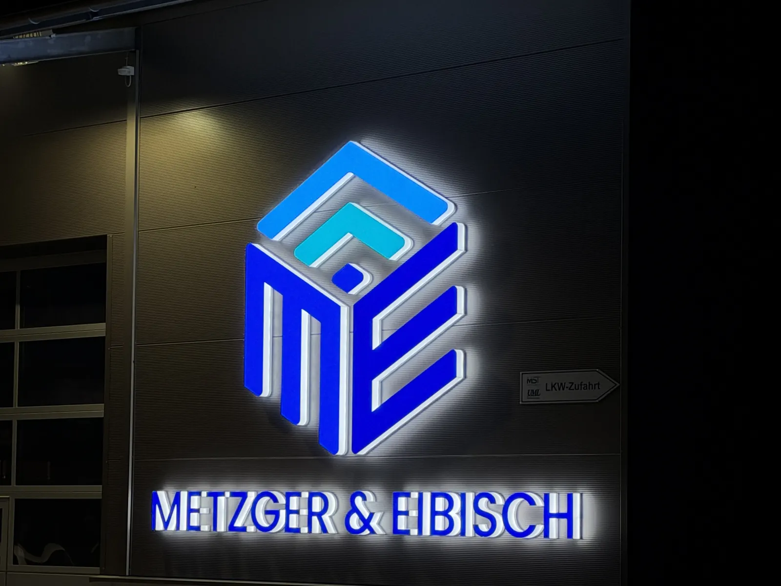 Beleuchtetes Firmenschild von Metzger & Eibisch bei Nacht